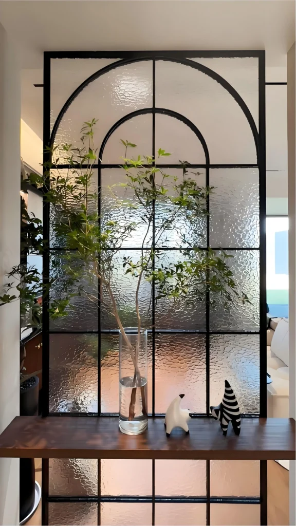 Modern black-framed glass partition with a floating wooden console shelf, creating an airy and layered luxury foyer design.