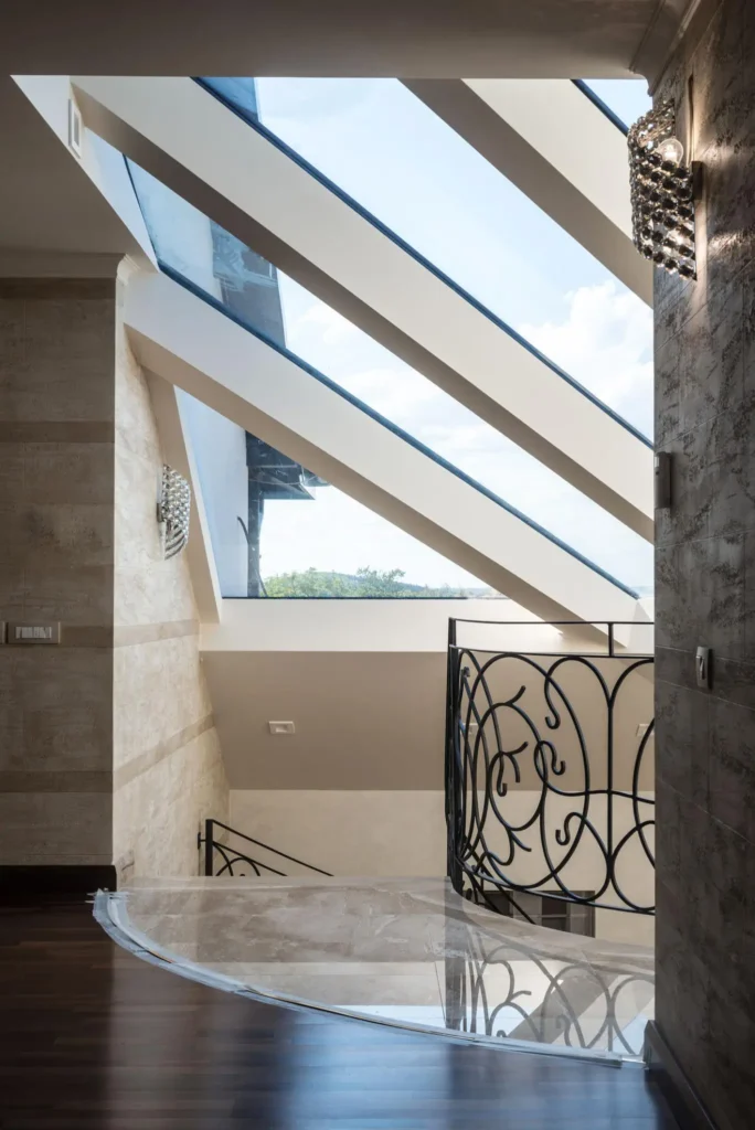 Custom architectural slanted skylights illuminating a luxury staircase with wrought iron railings and decorative wall sconces in a high-end villa.
