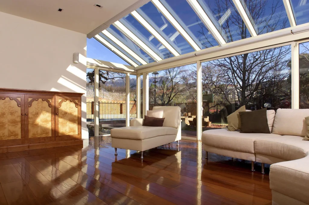 A luxurious living room flooded with natural sunlight from a large custom slanted glass skylight, showcasing glossy hardwood floors and modern furniture.