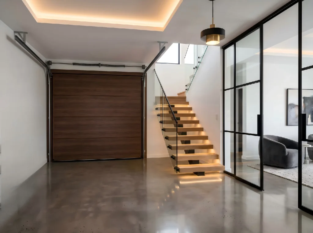 Luxury interior of an attached garage featuring a premium wood-finish insulated garage door, modern staircase, and cohesive aesthetic design.