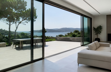 Large lift-and-slide glass door connecting a minimalist luxury villa living room to a sea-view terrace.