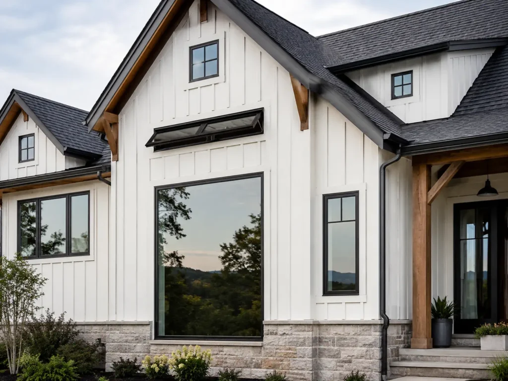 Modern farmhouse façade showing mixed window styles, minimalist grille patterns, black frames, white siding, timber accents, and stone base