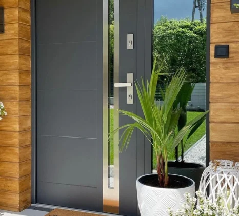 Modern dark grey cast aluminum exterior system door with a vertical glass insert and metal handle for luxury villas.